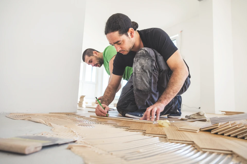 Deux artisans installent un parquet en bois massif dans une pièce aux murs blancs