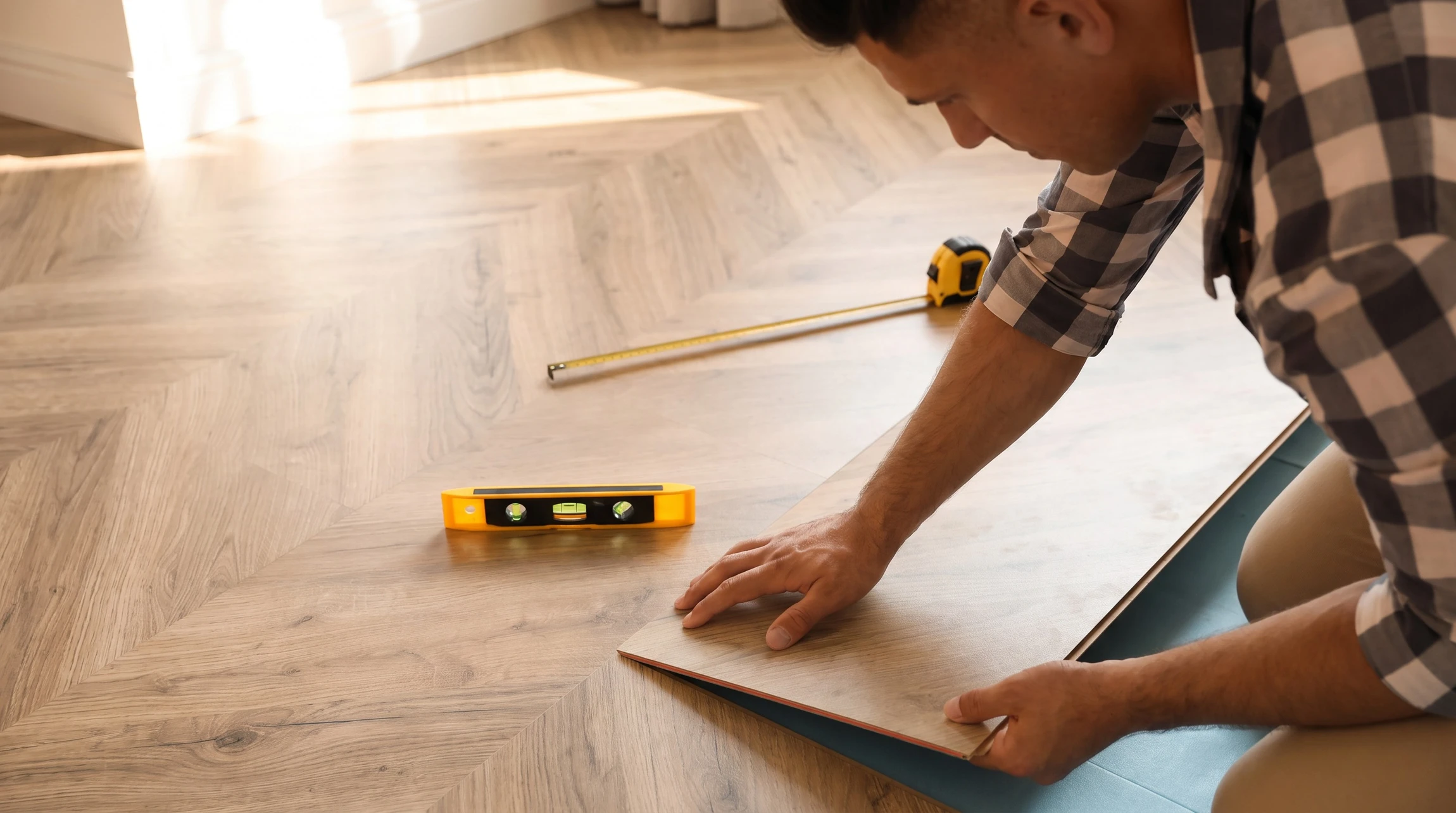 Artisan à genoux installant un parquet en chêne massif à chevrons dans un intérieur résidentiel